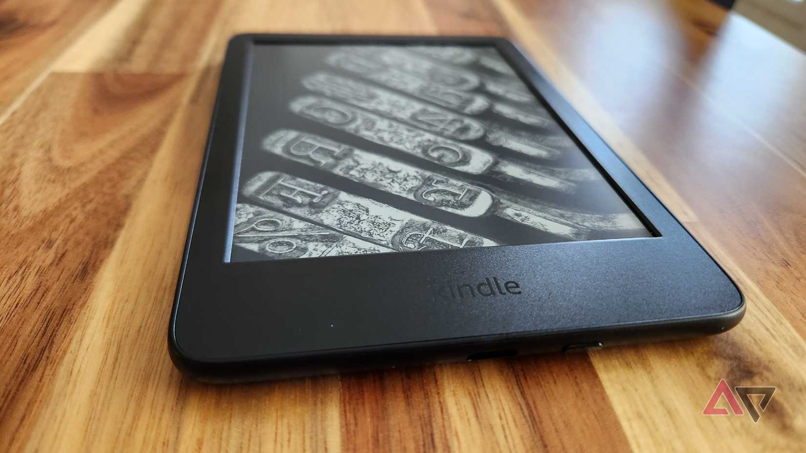A Kindle sits on a wooden table showing a screensaver of decorative letters