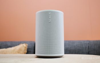 The Sonos Era 100 smart speaker on a table in front of an orange wall.